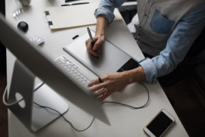 young male designer using graphics tablet while working with computer to design a ppt template